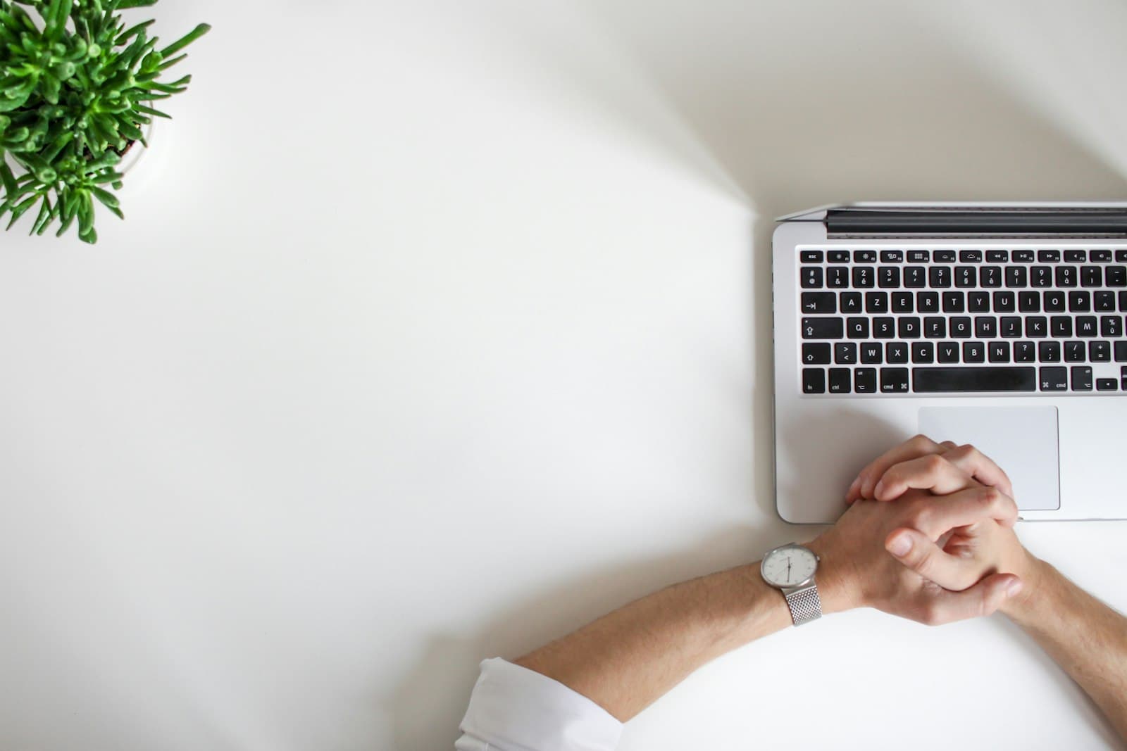 Hands resting on a laptop on a plain desk